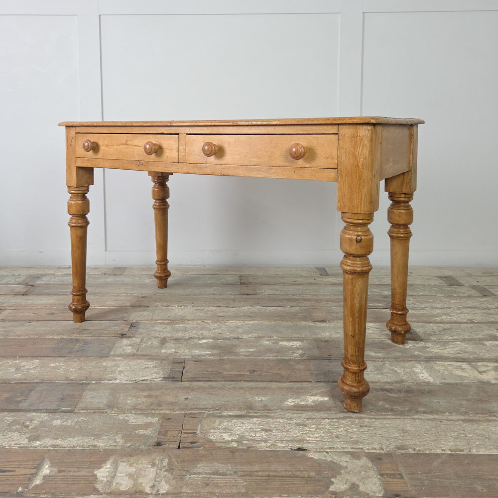 An antique pine console table from the late Victorian period, featuring decorative turned legs, two useful drawers, and a wax-sealed surface that enhances the natural warmth of the aged pine.

