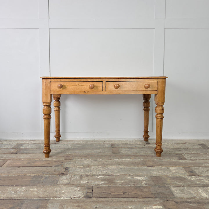 An antique Victorian pine table with a waxed patina, two front drawers, and classic turned legs. The piece combines rustic styling with functional proportions for versatile everyday use.

