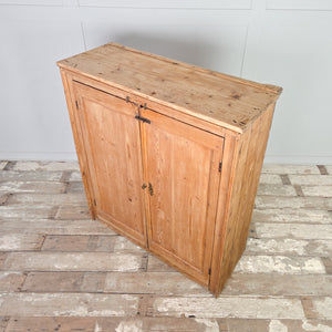 Antique Victorian pine cupboard with a simple plinth base, two opening doors, brass catches and bolt, and four fixed internal shelves behind the doors.
