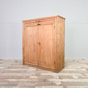 Pine cupboard dating to the 19th century, featuring panelled double doors, brass hardware, and a stripped pine finish with rustic farmhouse character.
