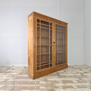 A Victorian-style antique pine glazed bookcase made from solid pine with a waxed finish. The double doors feature frosted glass panels and open to reveal adjustable shelving inside.
