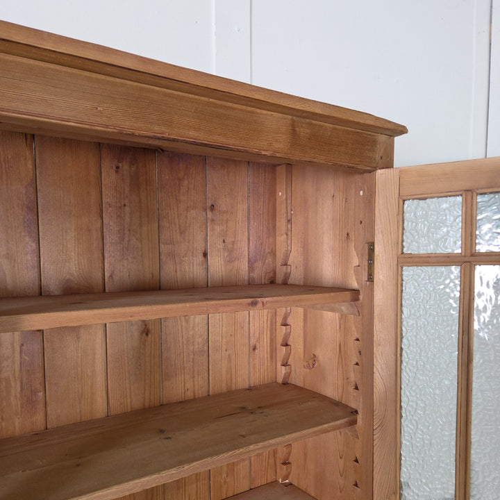 A tall antique pine glazed cupboard with four adjustable shelves behind full-length frosted glass doors. Made from solid pine and finished in wax, ideal for use in kitchens or dining spaces.

