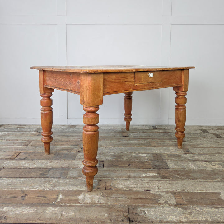 Antique farmhouse table in golden pine with drawer and turned leg base, featuring rich colour variation and natural wear across the plank top for a well-used, rustic look.

