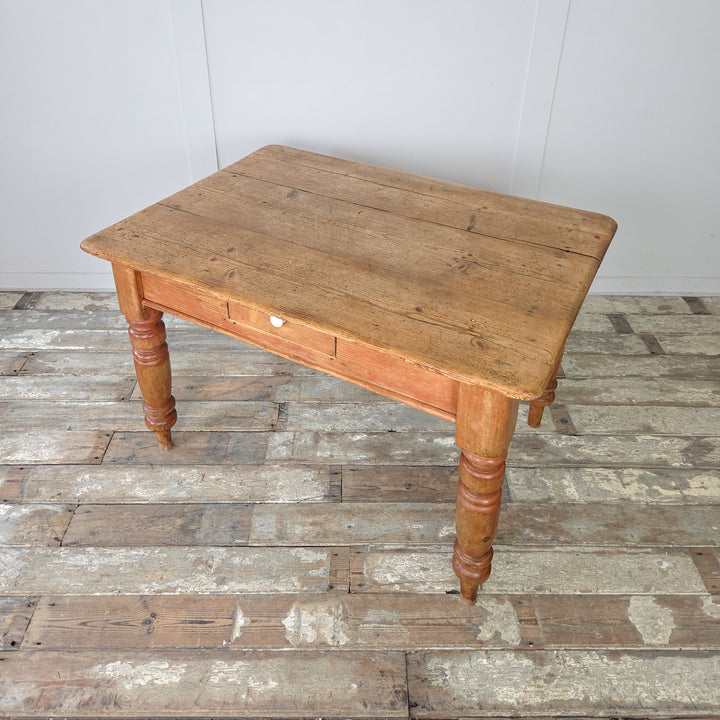 Antique four-seater pine kitchen table with classic proportions, worn plank top, and a drawer, suitable for small households or cottages with period or country interiors.
