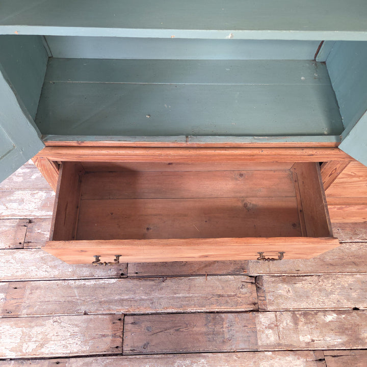 An antique 19th century English pine housekeeper’s cupboard of generous proportions, featuring a shelved upper section with panelled doors, a painted blue interior, and a base section with two drawers on a plinth base.