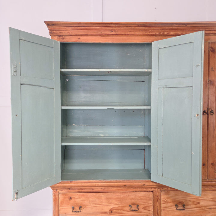 • A large antique Victorian English pine housekeeper’s cupboard with panelled upper doors, internal fixed shelving, two deep base drawers with decorative brass handles, a plinth base, and a moulded cornice top.
