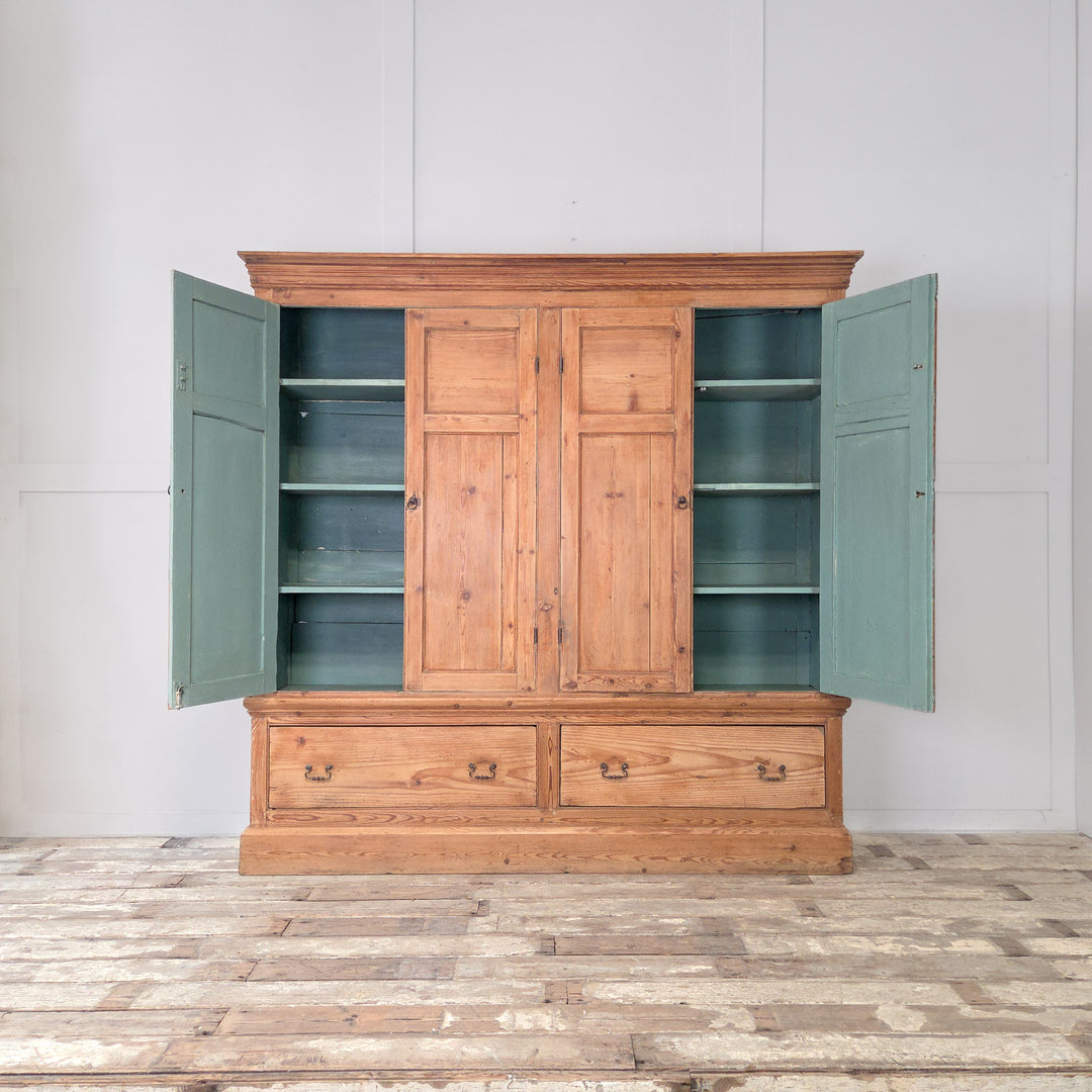 A 19th century Victorian housekeeper’s cupboard in solid English pine, of generous proportions, featuring two upper panelled cupboards with a soft blue painted interior above two large base drawers on a plinth base.