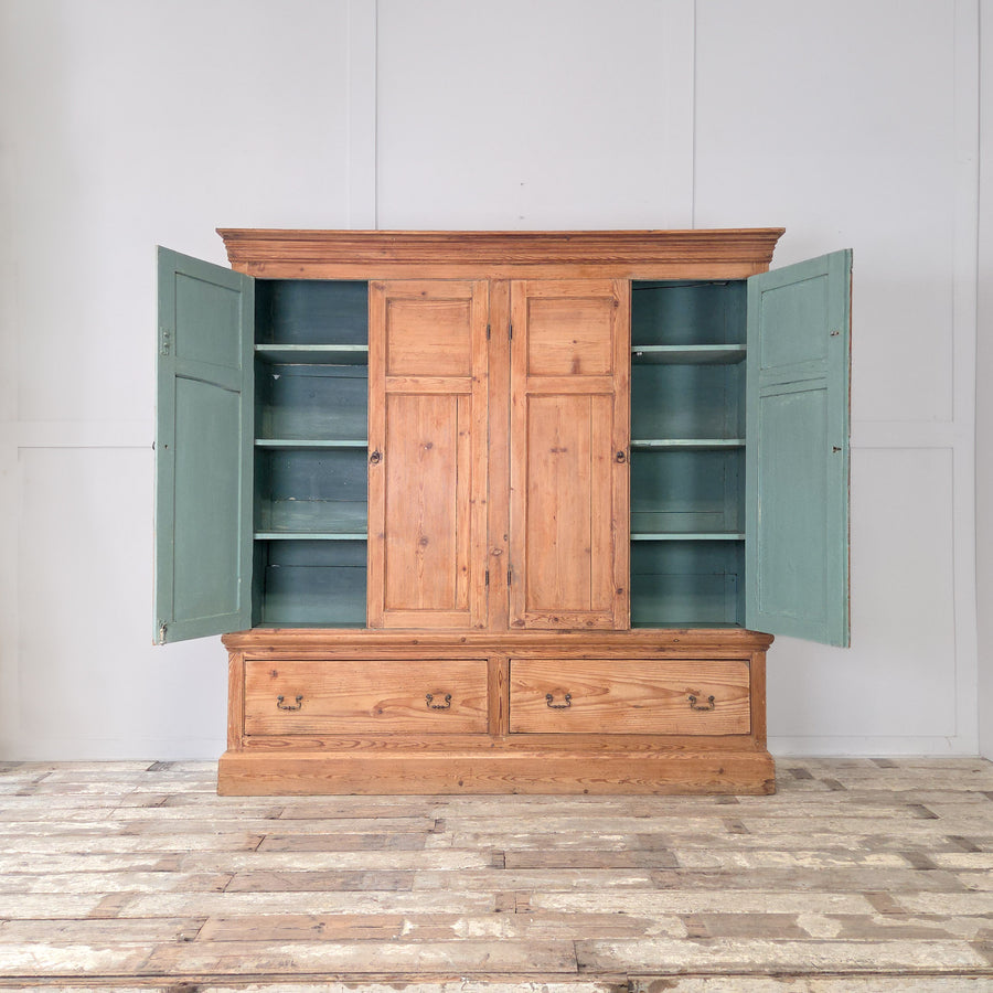 A 19th century Victorian housekeeper’s cupboard in solid English pine, of generous proportions, featuring two upper panelled cupboards with a soft blue painted interior above two large base drawers on a plinth base.