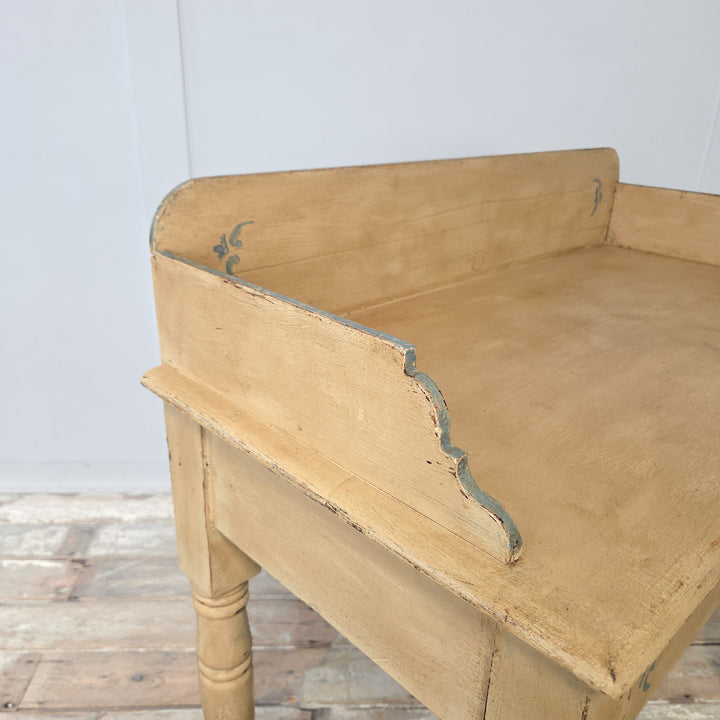 An antique Victorian painted pine console table, originally a 19th century washstand, with gallery back, shaped sides, four turned legs, and a lower display shelf, later painted in pale yellow with decorative pale blue trim for use in farmhouse or cottage interiors.