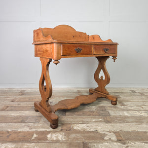 A rustic farmhouse-style Victorian pine washstand with a shaped gallery back, two drawers fitted with brass swan neck handles and a lower shelf. The pine surface is sealed with antique wax and the piece stands on shaped supports with ball feet.
