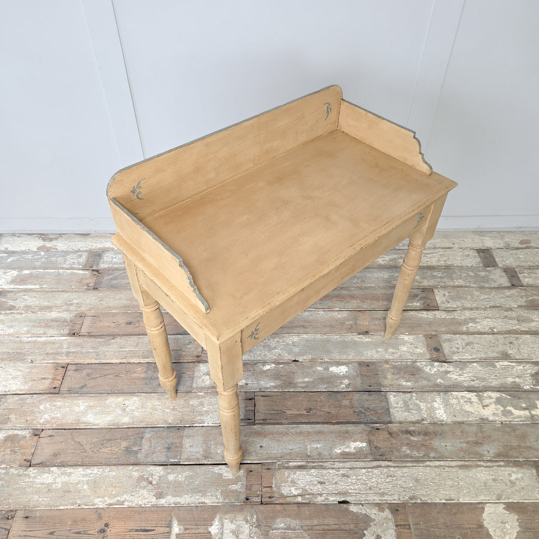 An antique painted pine washstand in the Victorian style, dating to the late 19th century, with a gallery back, shaped sides, four turned legs, and a lower shelf, finished in pale yellow paint with pale blue detailing, suitable for use as a console table in country interiors.