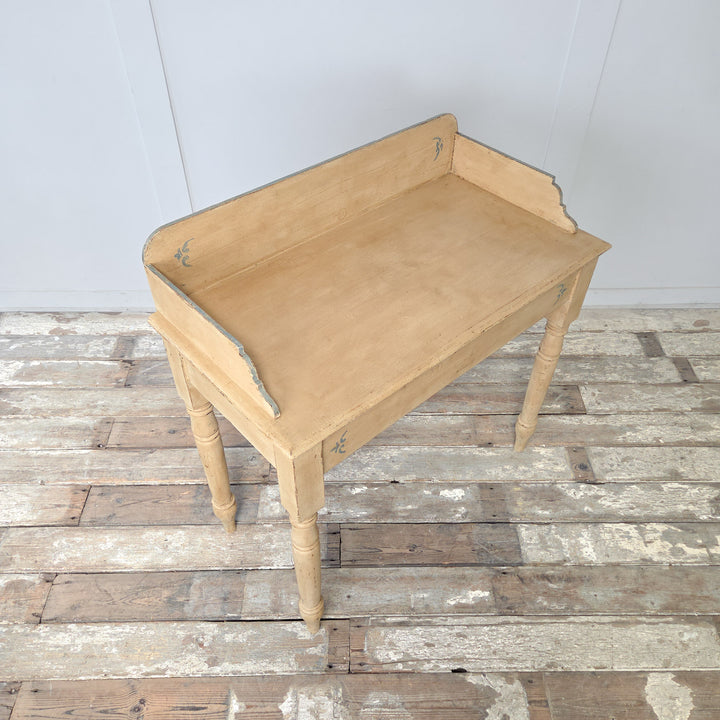An antique painted pine washstand in the Victorian style, dating to the late 19th century, with a gallery back, shaped sides, four turned legs, and a lower shelf, finished in pale yellow paint with pale blue detailing, suitable for use as a console table in country interiors.