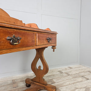 An antique pine washstand from the Victorian period, featuring a shaped gallery back, twin drawers and a lower shelf. The drawers have brass swan neck handles and the washstand is raised on shaped supports with ball feet.