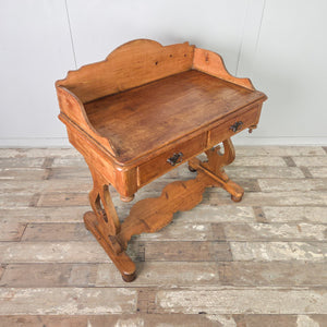 A late 19th century farmhouse-style pine washstand with a shaped gallery back, two drawers and a lower shelf. The waxed pine finish enhances the natural grain, and the piece stands on shaped supports with ball feet.