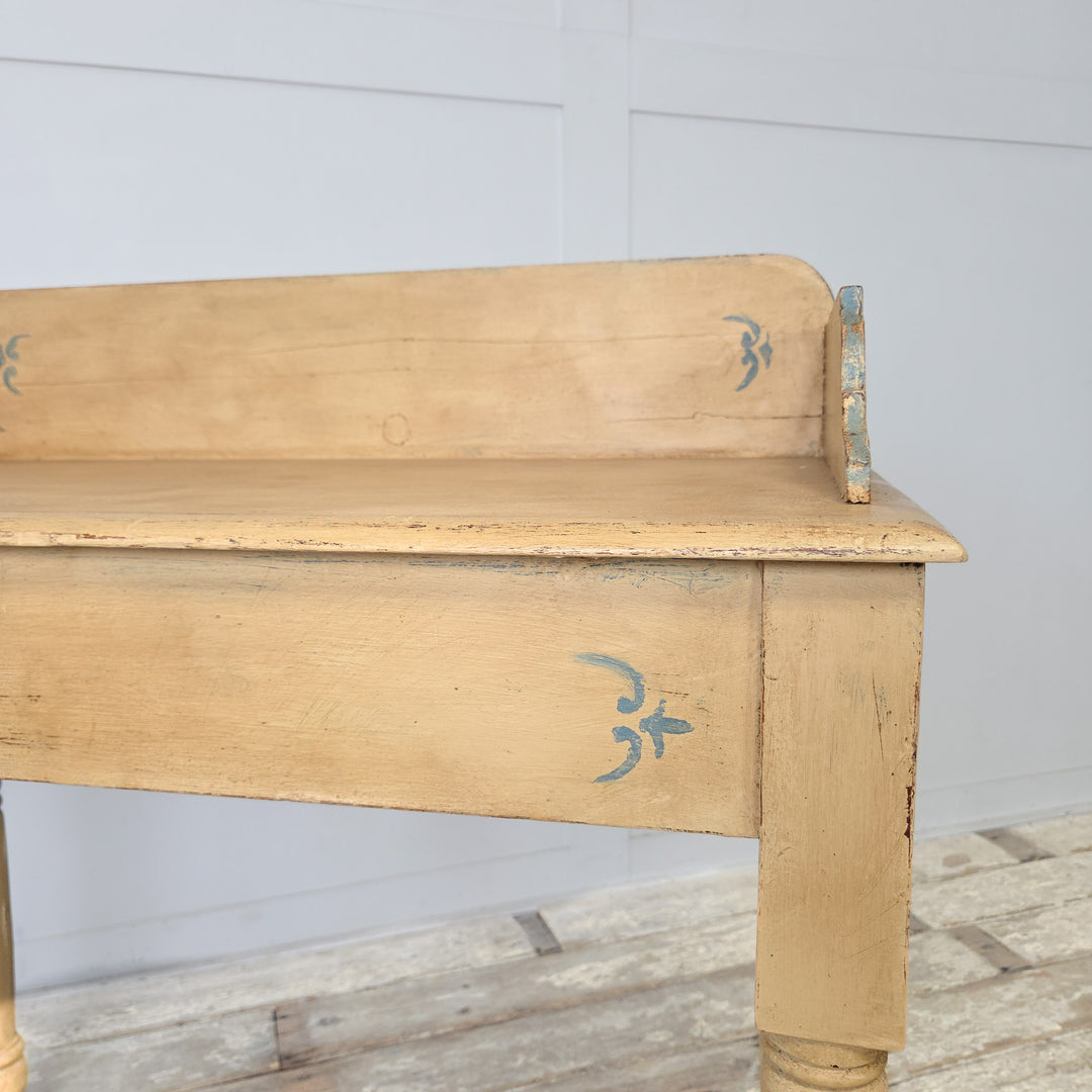 A 19th century antique Victorian painted pine washstand, later adapted with pale yellow paint and blue trim, featuring a shaped gallery back, four turned legs, and a lower shelf, perfect for use as a small console table in farmhouse-inspired interiors.