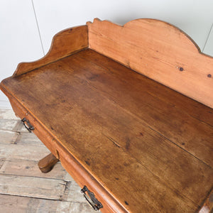 A country-style antique Victorian pine washstand featuring a shaped gallery back, two drawers with brass swan neck handles and a lower shelf. The solid pine construction is finished in antique wax and raised on shaped supports.