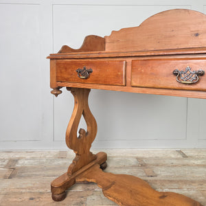 A rustic antique pine washstand from the late 19th century, with a shaped gallery back running around the back and sides, two drawers and a lower shelf. The washstand is finished in waxed pine and stands on shaped supports with ball feet.