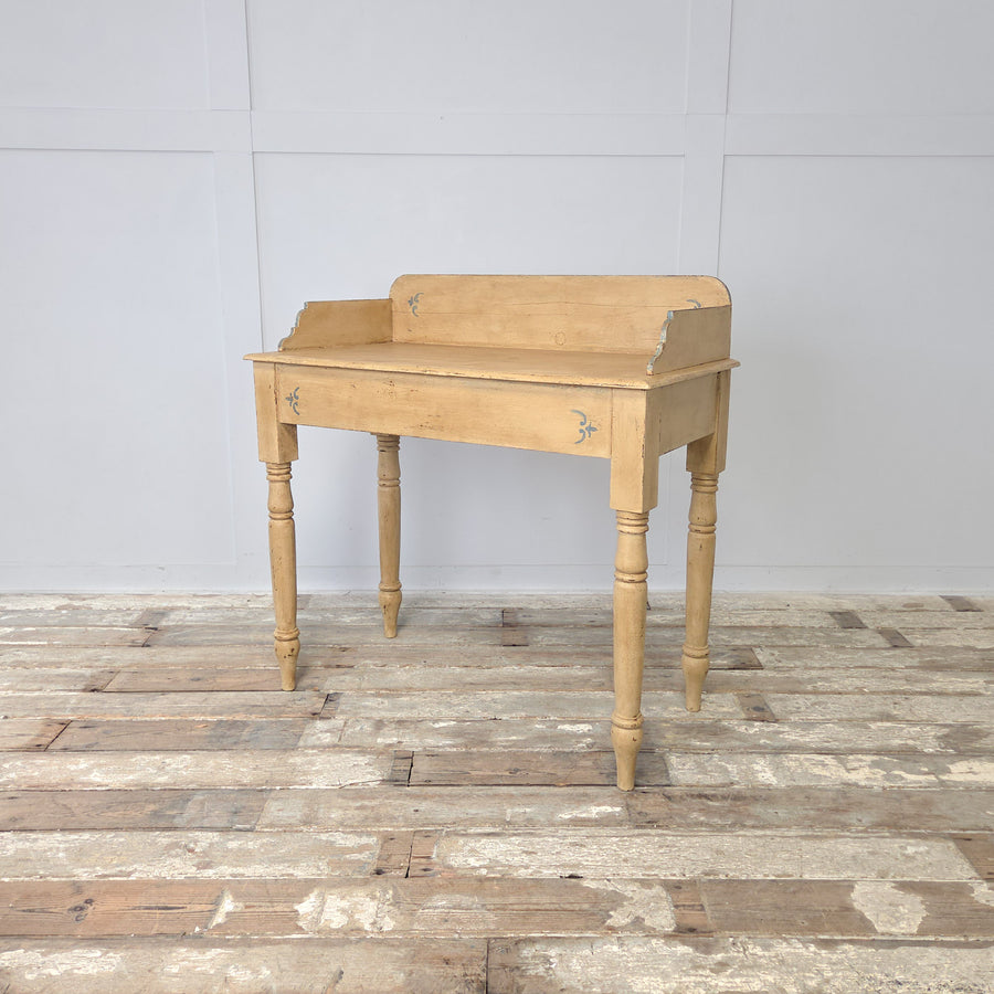 A late 19th century Victorian painted pine washstand, also suited as a console table, with gallery back and shaped sides, raised on four turned legs with a lower display shelf, finished in pale yellow paint with decorative pale blue trim and flourishes, ideal for use in a farmhouse hallway, bedroom, or bathroom.