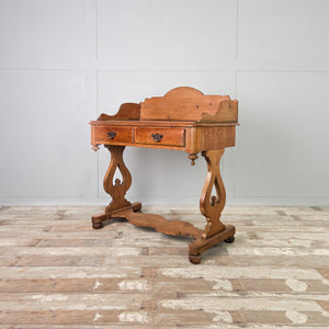 A country-style antique pine washstand dating to the late 19th century, with a shaped gallery back, two drawers and a lower shelf. The waxed pine finish highlights the grain, and the piece is raised on shaped supports with ball feet.
