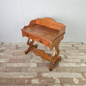 A rustic farmhouse-style pine washstand from the Victorian period, featuring a shaped gallery back, two drawers with brass swan neck handles and a lower shelf. The piece is finished in antique wax and stands on shaped supports.