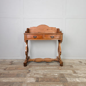 An antique pine washstand with country and cottage character, featuring a shaped gallery back, two drawers and a lower shelf. The drawers have brass swan neck handles, and the washstand is raised on shaped supports with ball feet.