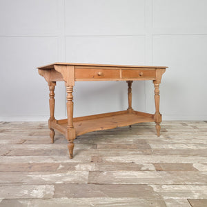 An antique pine washstand from the Victorian period with two drawers and a shaped lower shelf, raised on four turned legs and finished in clear wax. The light pine patina gives it a rustic farmhouse and country character, suitable for use as a hall table, console table or dressing table.