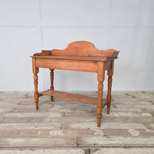 A Victorian antique pine washstand from the 19th century, featuring a decorative gallery back with scroll sides, turned legs and a shaped lower shelf. Ideal as a farmhouse console or side table, this antique retains its waxed pine patina and versatile country house character.