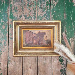 Victorian oil painting on board featuring a rural landscape with a rustic country building, rendered in muted colours and gentle brushstrokes. The artwork is presented in a decorative gilt frame and offers authentic period style for traditional interiors.