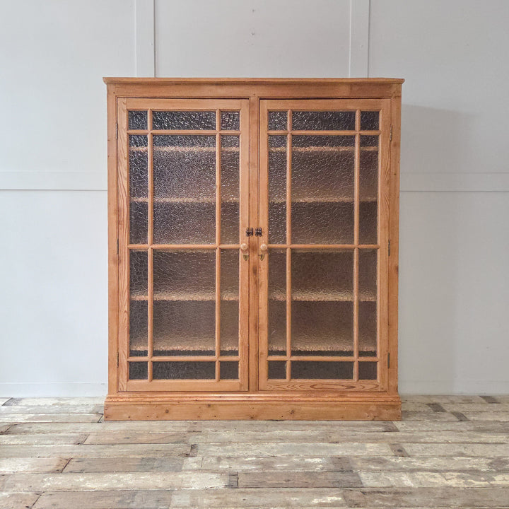 A well-built antique pine glazed bookcase with a waxed finish and solid pine frame. The frosted glazed doors open to reveal adjustable internal shelving, ideal for home offices or living spaces.