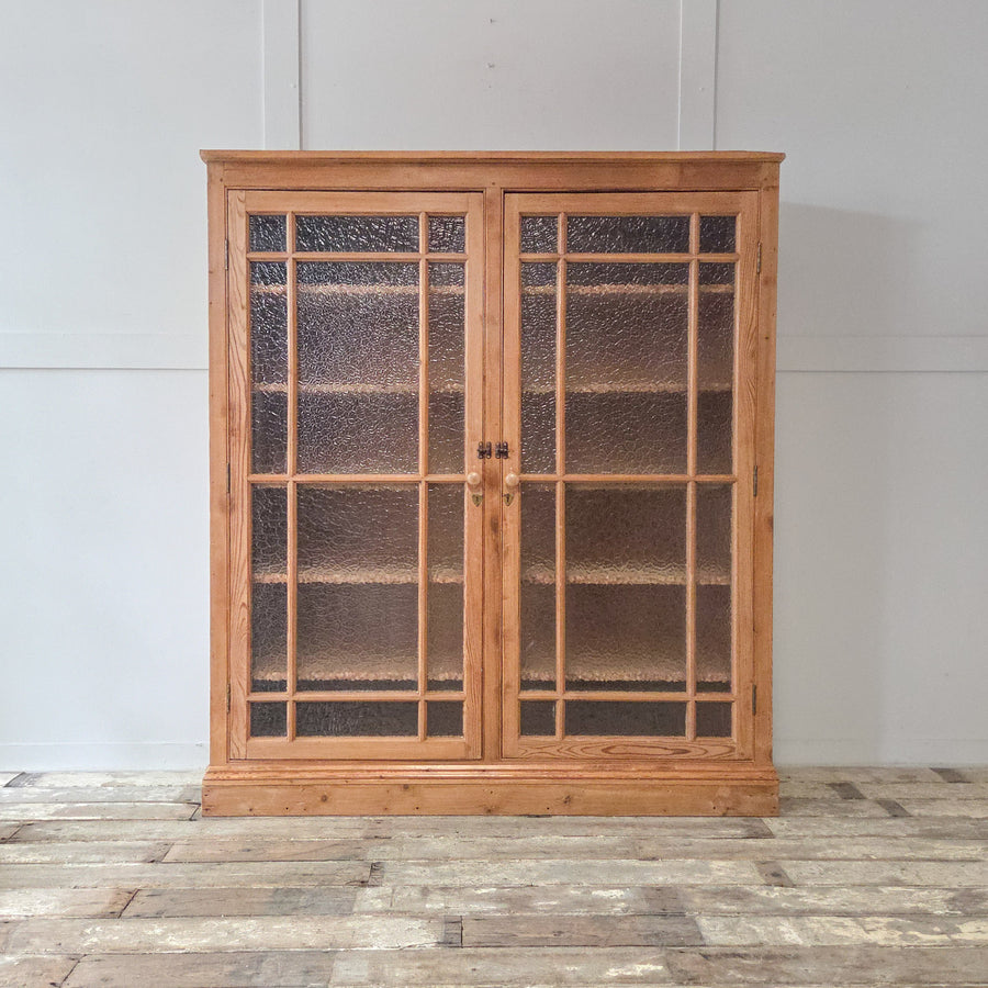 A well-built antique pine glazed bookcase with a waxed finish and solid pine frame. The frosted glazed doors open to reveal adjustable internal shelving, ideal for home offices or living spaces.