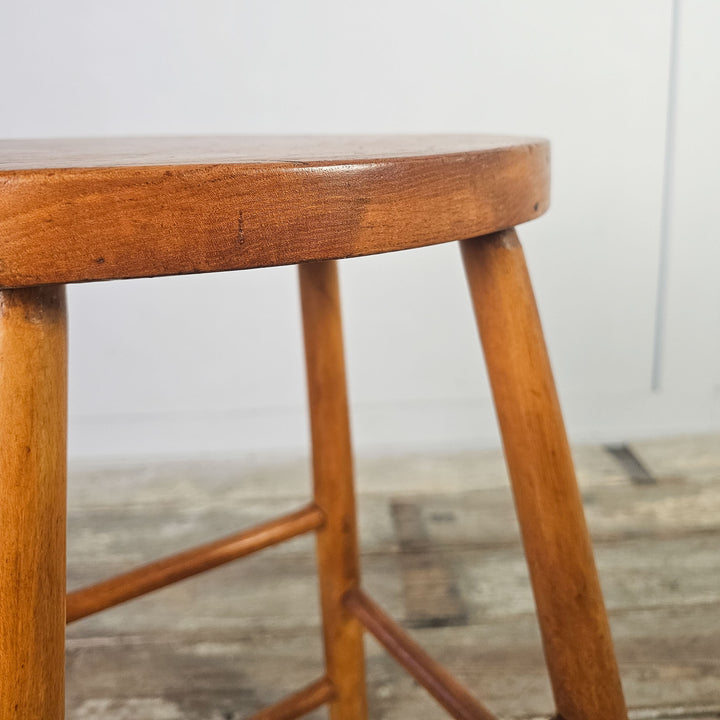 Mid-century school stool in elm with oval seat and leg stretchers.

