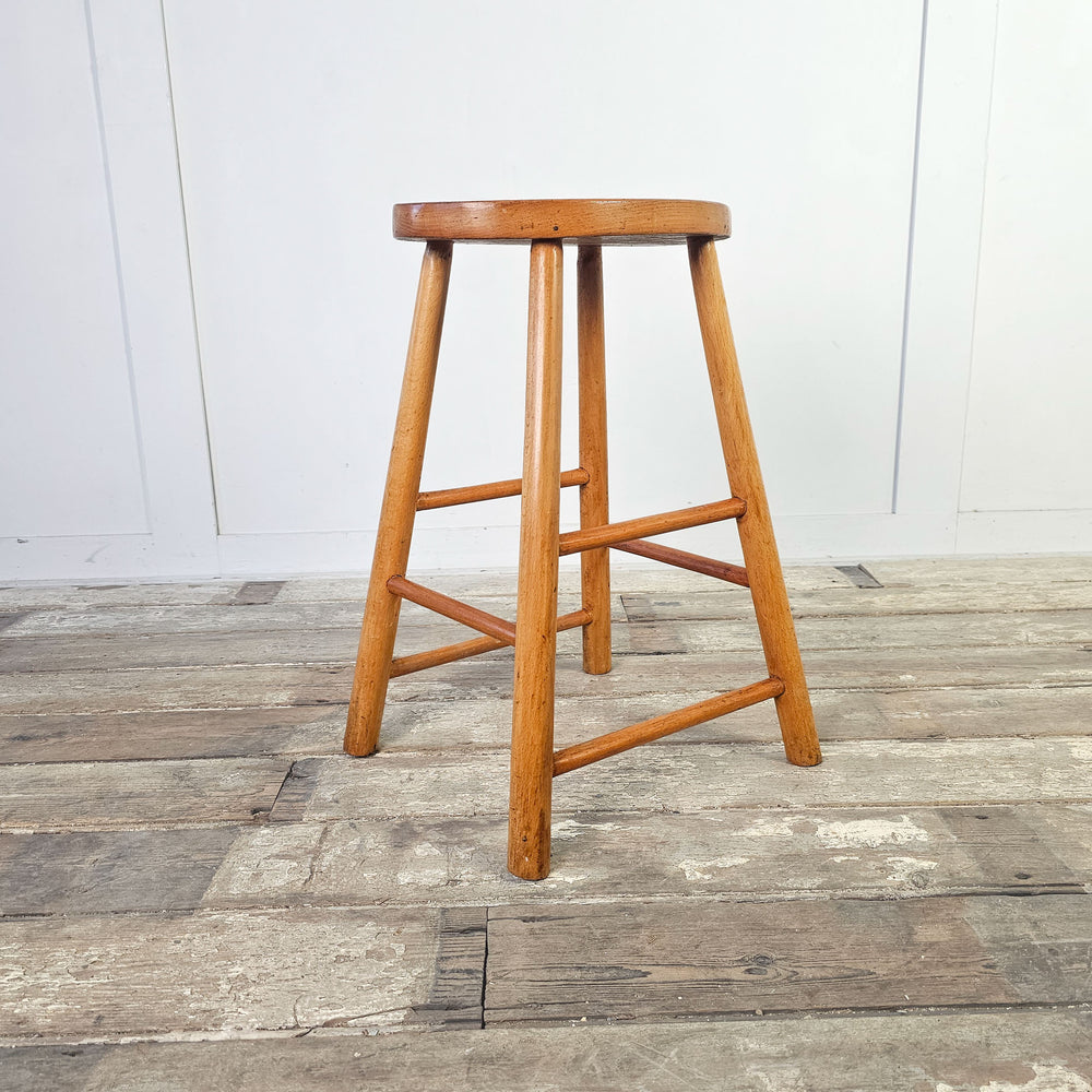 Mid-century school stool in elm with oval seat and leg stretchers.
