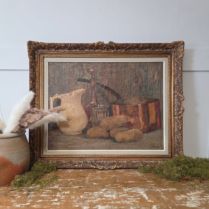 Original vintage Belgian still life oil painting from circa 1940, featuring a rustic arrangement of pottery jug, glass, decanter, potatoes, and a copper pan. Set in a decorative wooden frame and signed by Bertha Lombet, this artwork suits classic and modern interiors.
