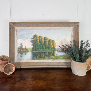 A vintage French landscape oil painting on board from the 20th century, depicting a serene rural scene with a still pond, tall trees, meadowland, and distant fields, all set within a rustic painted wooden frame. Original artwork in soft greens, blues, and earthy tones, ready to hang as wall décor.