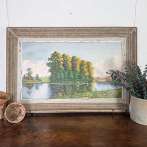 An original 20th century vintage oil painting on board showing a French countryside landscape with reflective pond, wildflowers, and tree line, framed in a distressed painted wooden surround. This signed painting combines decorative charm with a natural palette of greens and blues, perfect for rustic interiors.