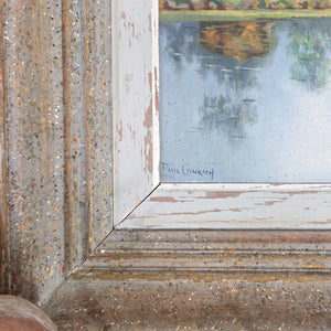 A framed vintage French landscape oil painting on board, painted during the 20th century, showing a tranquil countryside scene with pond, trees, and meadow under soft sky. The painting is mounted in a painted wooden frame with time-worn patina, ready to hang as original wall art for rustic interiors.