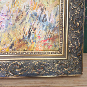 An oil on board vintage landscape painting housed in a decorative gilt frame. The composition shows a rural country house scene with outbuildings, meadow grasses in warm yellows and oranges, and rolling hills in deep greens. A naïve style work that captures the charm of the British countryside.