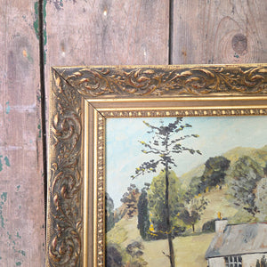Rustic countryside vintage oil painting on board, presented in a gilt frame. The subject shows a large house with barns and outbuildings surrounded by meadowland, with hills rising beyond. Golden yellows, bright oranges and green tones create a warm palette across this decorative wall art.