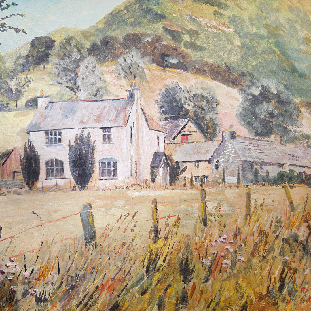 20th century vintage oil painting on board in naïve style, depicting a rural country house and adjoining outbuildings in a meadow. Behind, rolling green hills and moody trees form the landscape. Set within a gilt frame, the warm tones of yellow, orange and green make it an appealing decorative piece.