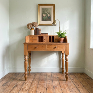 A rustic pine vintage desk with four turned legs, two front drawers and a gallery top fitted with pigeonholes, four small drawers and a tiny cupboard. Its compact cottage style layout offers practical storage in a small footprint.