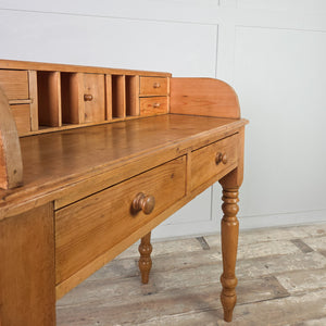 A vintage pine side table in a rustic farmhouse style, featuring four turned legs, two front drawers and a gallery top. The upper section includes pigeonholes, four small drawers and a tiny cupboard for organised storage.