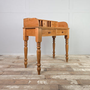 A compact vintage pine desk with a cottage style gallery top fitted with pigeonholes and small drawers. Supported by four turned legs with two apron drawers below, creating a practical, space-efficient layout.