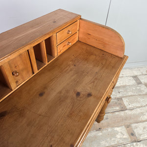 A farmhouse style vintage pine console table with two drawers, turned legs and a gallery back incorporating pigeonholes, four small drawers and a tiny cupboard. The rustic pine finish provides functional, organised storage.