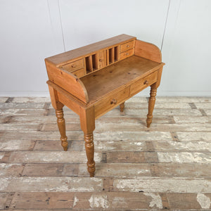 A vintage pine dressing table with a rustic pine finish, four turned legs and two lower drawers. The gallery section contains pigeonholes, four miniature drawers and a tiny cupboard, offering varied storage options.