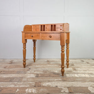 A rustic pine vintage side table with two drawers to the apron and a gallery top featuring pigeonholes and small drawers. The turned legs and compact proportions create a cottage style piece suited to everyday use.
