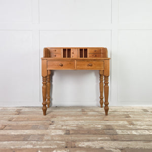 A cottage style vintage pine console table with turned legs and a gallery back. Two drawers sit below, while the top incorporates pigeonholes and four small drawers around a tiny central cupboard for additional storage.