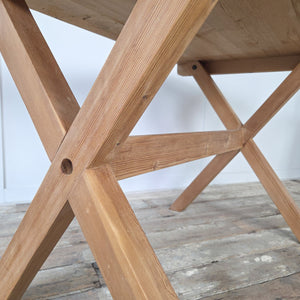 Rustic vintage pine X-frame trestle table with stripped pine finish, sealed in wax to protect the surface. The thick rectangular top displays the natural grain of the wood. A versatile farmhouse style table suitable for kitchens, hallways, or studies, used as a dining table, desk, or console.
