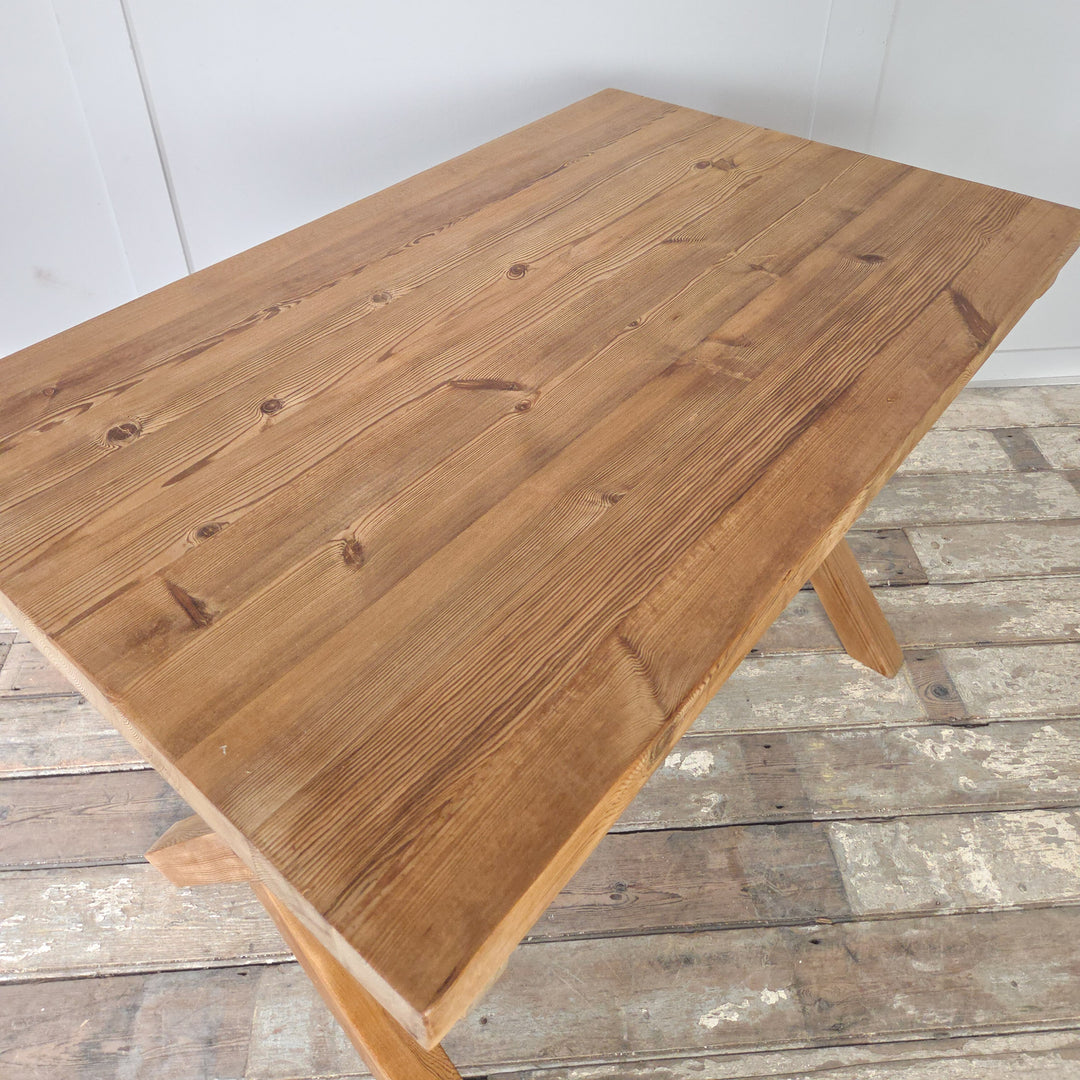 Vintage pine trestle table with stripped and waxed pine finish, showing natural grain. The X-frame base gives strength and visual interest, supporting a thick rectangular top. This farmhouse style table offers multiple uses, from dining to working, or as a rustic console in the home.
