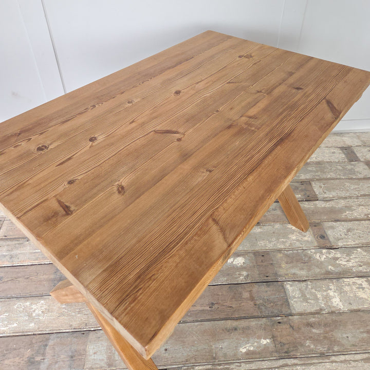 Vintage pine trestle table with stripped and waxed pine finish, showing natural grain. The X-frame base gives strength and visual interest, supporting a thick rectangular top. This farmhouse style table offers multiple uses, from dining to working, or as a rustic console in the home.