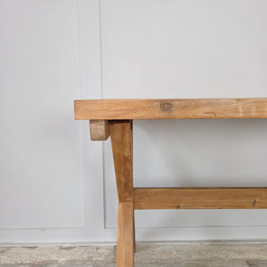 A vintage pine trestle table with stripped pine patina, sealed in clear wax for durability. Its thick rectangular top and distinctive X-frame base provide both strength and character. A farmhouse style table that works well as a dining table, office desk, or decorative console in living spaces.
